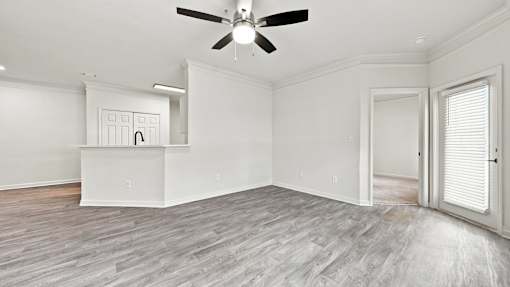 A room with a ceiling fan and light fixture, a white cabinet with a black handle, and a wooden floor.