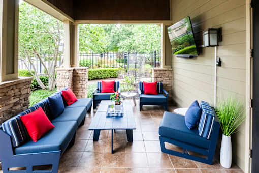 A patio with blue couches and pillows, a coffee table, and a flat screen TV mounted on the wall.