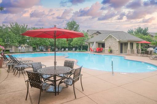 A red umbrella is in front of a pool and a house.