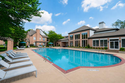 A large swimming pool surrounded by lounge chairs and a building in the background.