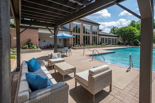 A patio with a couch and chairs under a roof next to a pool.