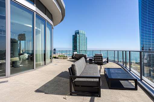 A black sofa and table are on a balcony with a view of the city.