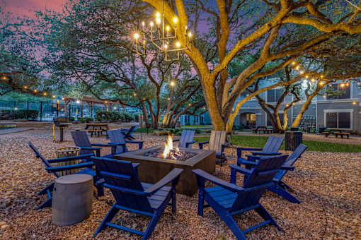 A fire pit surrounded by blue chairs in a gravel area.