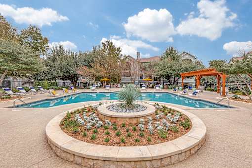 A pool surrounded by a circular flower bed with a palm tree in the middle.