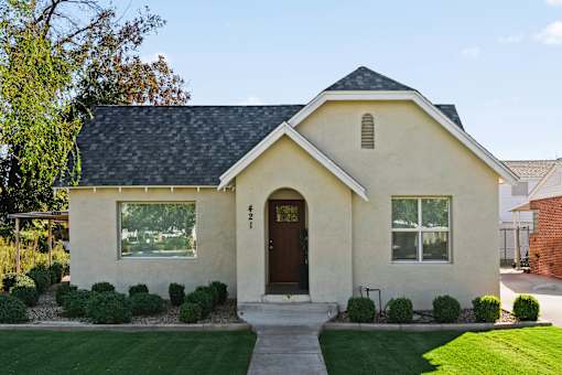A small house with a brown door and windows surrounded by greenery.