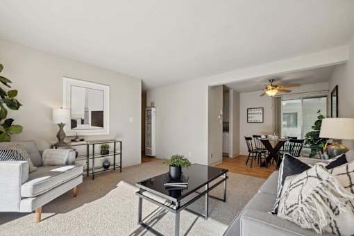 A living room with a grey couch, a black coffee table, and a dining area in the background.
