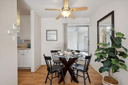 A dining room with a table set for two and a plant on the side table.