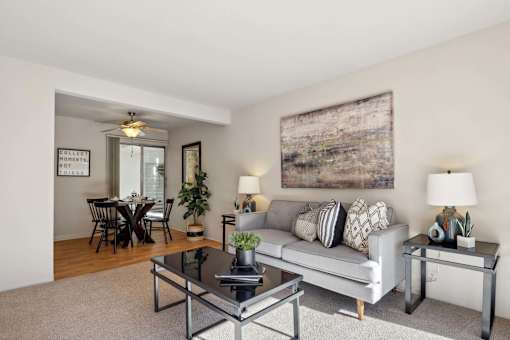 A living room with a grey couch, a glass coffee table, and a large abstract painting on the wall.