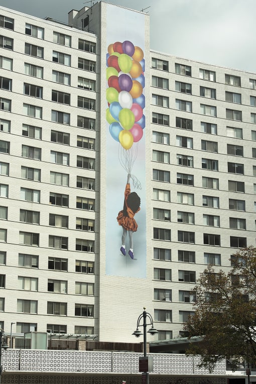 a mural of a girl holding balloons is shown on the side of an apartment building