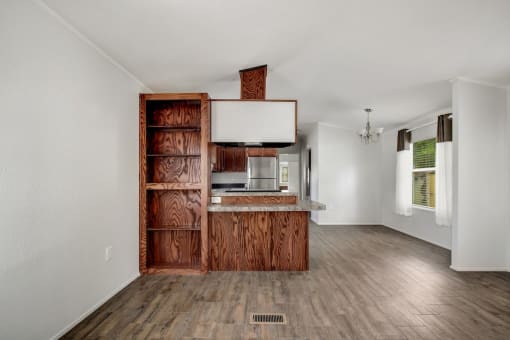 an empty living room with a kitchen in the background