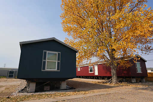 a black house with a red house behind it next to a tree at Country Lane, Cheyenne, WY