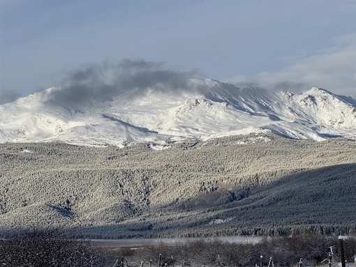 A mountain range covered in snow with a cloud of smoke rising from the peak.