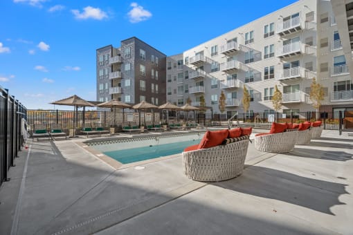 a pool with red chairs and umbrellas in front of an apartment building