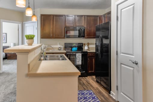 Westerville, OH Apartments for Rent - Kenyon Square - Kitchen with Beige Counters, Custom Cabinetry, Black Appliances, Modern Light Fixtures, and Wood-Style Flooring