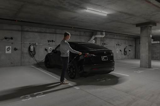 A man is charging an electric car in a parking garage.
