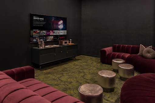 A room with a red couch and ottoman in front of a black wall with a poster on it.