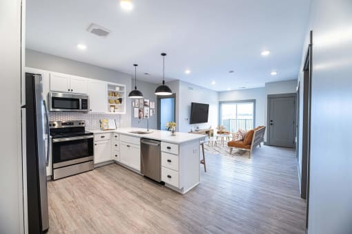 a kitchen and living room with white cabinets and stainless steel appliances at The Commons at Rivertown, Grandville, Michigan, 49418