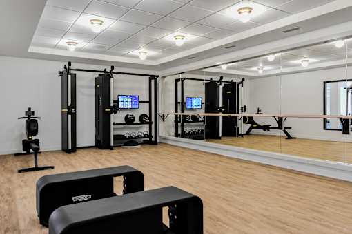 A gym with a variety of equipment including a treadmill, a stationary bike, a rowing machine, a squat rack, a bench press, a cable machine, a leg press, a pull up bar, a