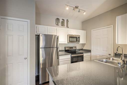 A kitchen with a refrigerator, microwave, oven, and sink.