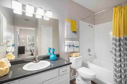 A bathroom with a white toilet, a sink, and a yellow shower curtain.