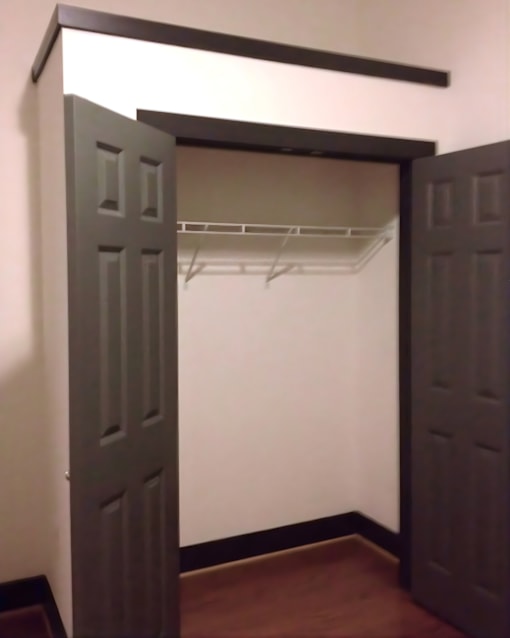 A white closet with a brown floor and two doors.