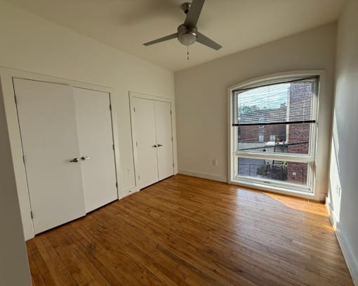 A room with a ceiling fan and a window showing a view of a building outside.