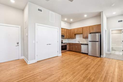 an empty kitchen with wood flooring and a stainless steel refrigerator