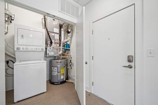 A white door is open to a hallway with a washer and dryer in the background.