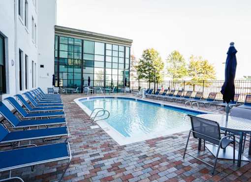 A pool surrounded by chairs and a building with a glass facade.