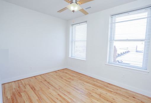 A room with wooden flooring and two windows.
