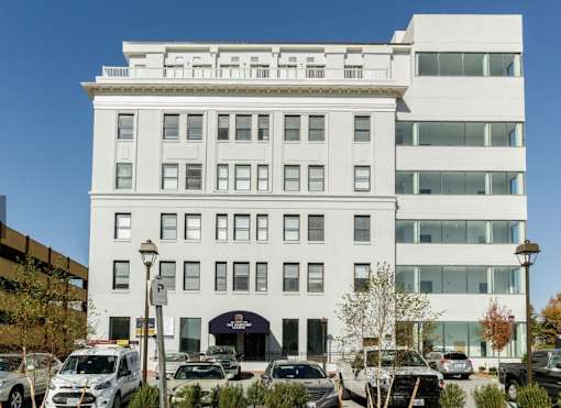 A white building with a black awning and cars parked in front.