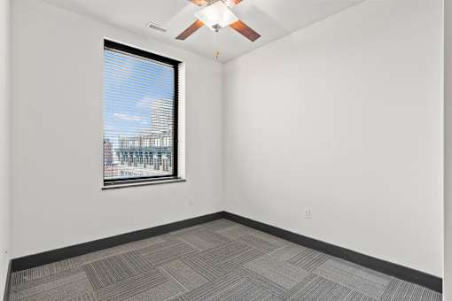 A room with a ceiling fan and a window overlooking a cityscape.