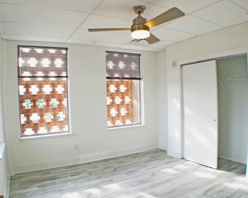 A room with a ceiling fan and two windows.