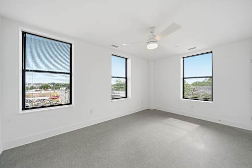 A spacious room with three windows and a ceiling fan.