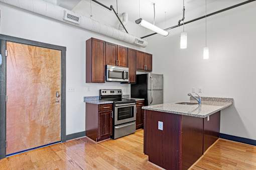 A kitchen with wooden floors and a refrigerator, microwave, oven, and sink.