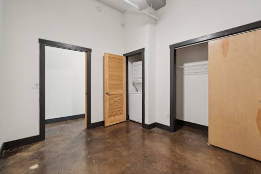 A room with a white wall and a door on the left and a white fridge in the middle.