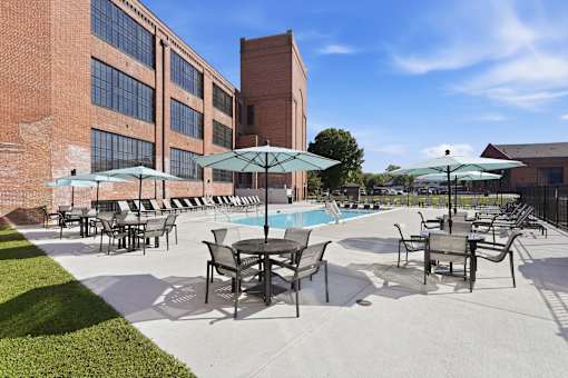 A pool area with chairs and umbrellas in front of a brick building.