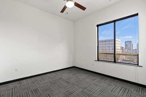 A room with a ceiling fan and a window overlooking a cityscape.