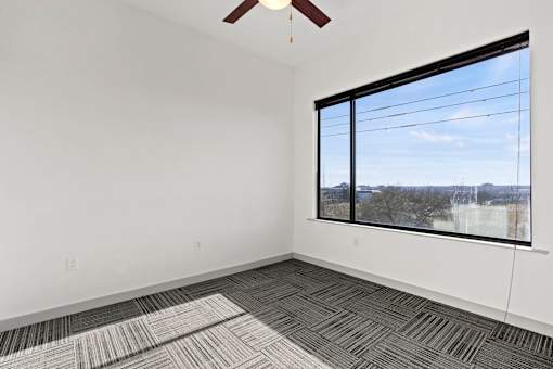 A room with a ceiling fan and a large window overlooking a cityscape.