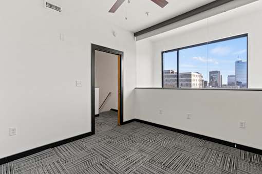 A room with a carpeted floor and a large window overlooking a cityscape.