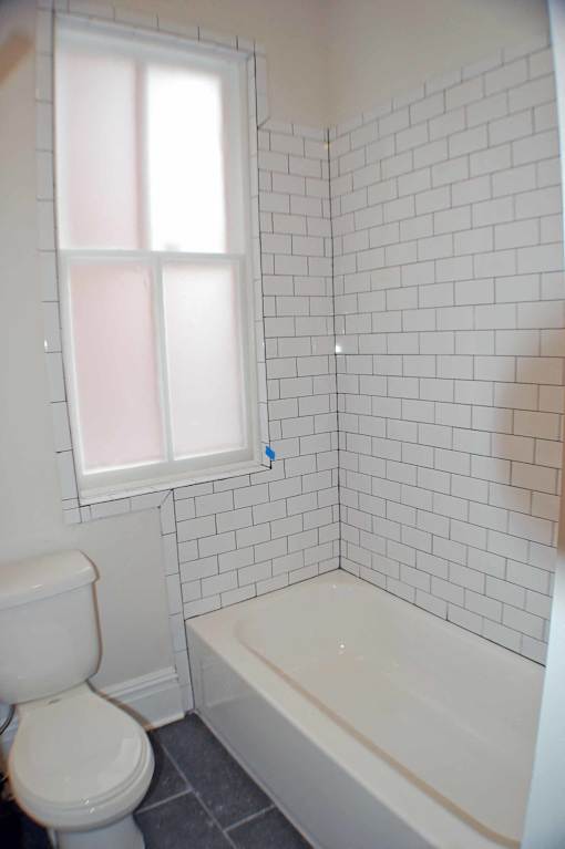 A white toilet sits next to a bathtub in a bathroom with white tiles.