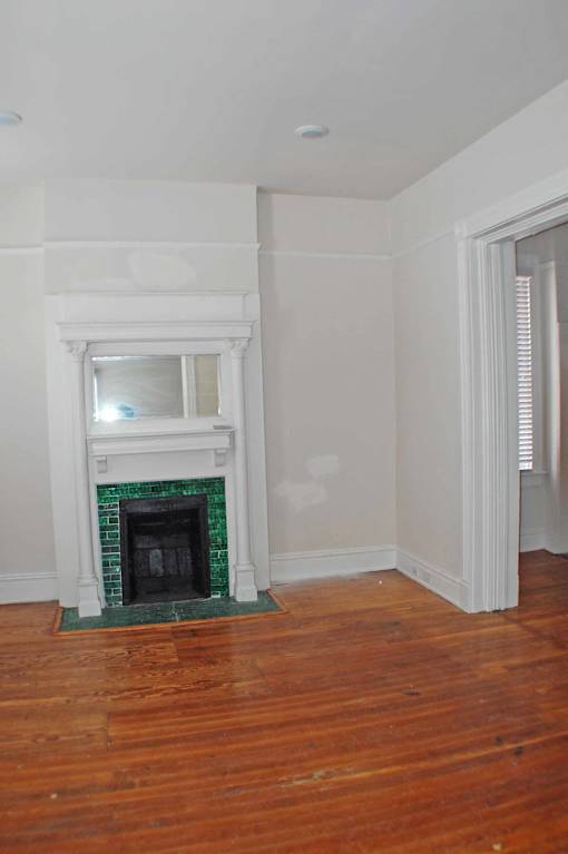 A fireplace with a green border sits in a room with wooden floors.