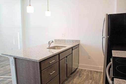 A kitchen with a black refrigerator and a sink with a granite countertop.