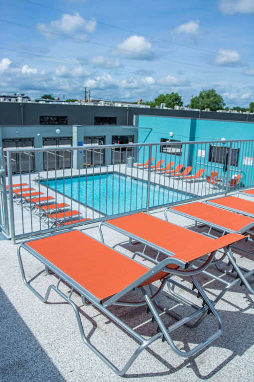 A pool with orange sun loungers and a blue sky.