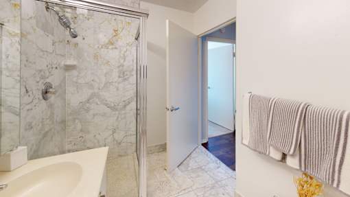 A bathroom with a marble shower, white sink, and a towel rack at 10 West Apartments, Long Beach, NY, 11561