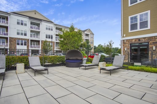 a large stone patio with three lounge chairs and a fire pit in front of an apartment building