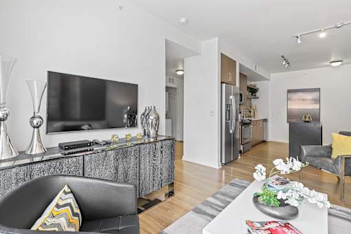 a living room with a large tv and a kitchen in the background at 8000 Uptown Apartments, Broomfield, CO