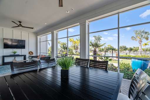 a patio with a wooden table and chairs and large windows at Artesia at Lakewood Ranch Apartments, Bradenton, FL
