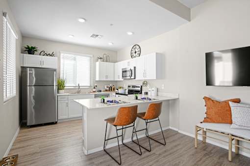 an open kitchen and living room with a white counter top and a stainless steel refrigerator at Soleil at Canyon Trails Apartments, Goodyear, Arizona