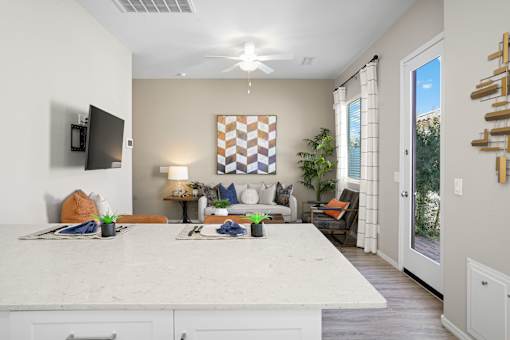 a kitchen island with a white counter top in front of a living room at Soleil at Canyon Trails Apartments, Arizona